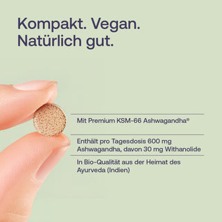 Hand hält kleine runde Ashwagandha-Tablette, hellgrüner Hintergrund, Text: Kompakt. Vegan. Natürlich gut.