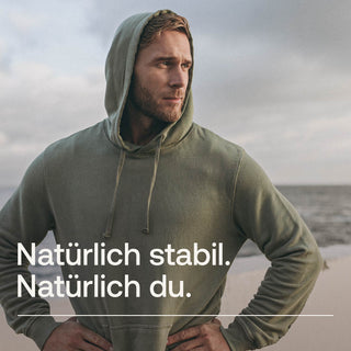 Mann in olivgrünem Hoodie am Strand - natürliche Stabilität und Gesundheit für aktive Menschen